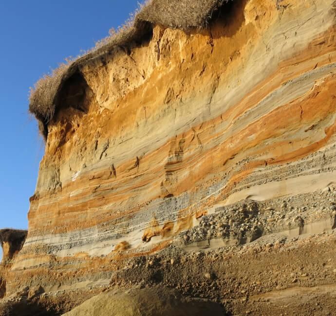 Exposed cliff face showing bands of orange, grey and cream sedimentary rock layers