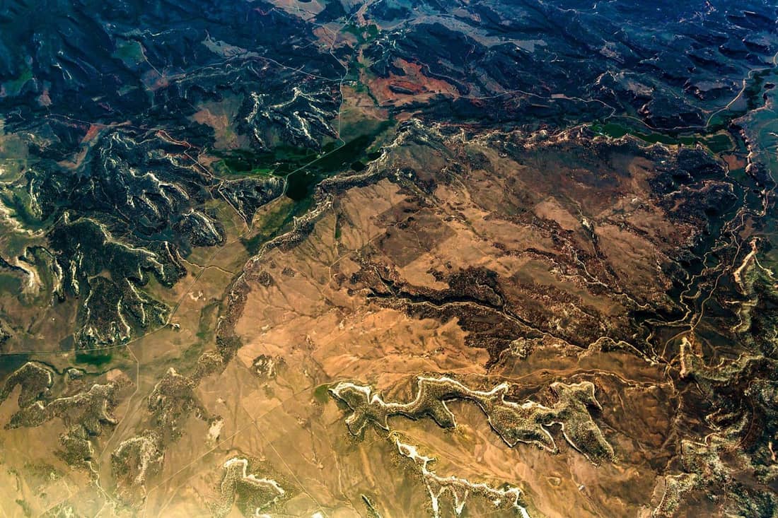 Aerial view of eroded terrain showing ridges, drainages and bare ground in shades of brown and green