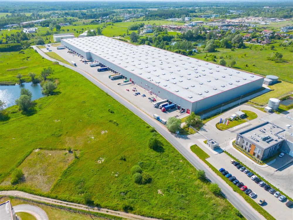 Aerial view of a large industrial warehouse with loading docks, a retention pond and surrounding open land